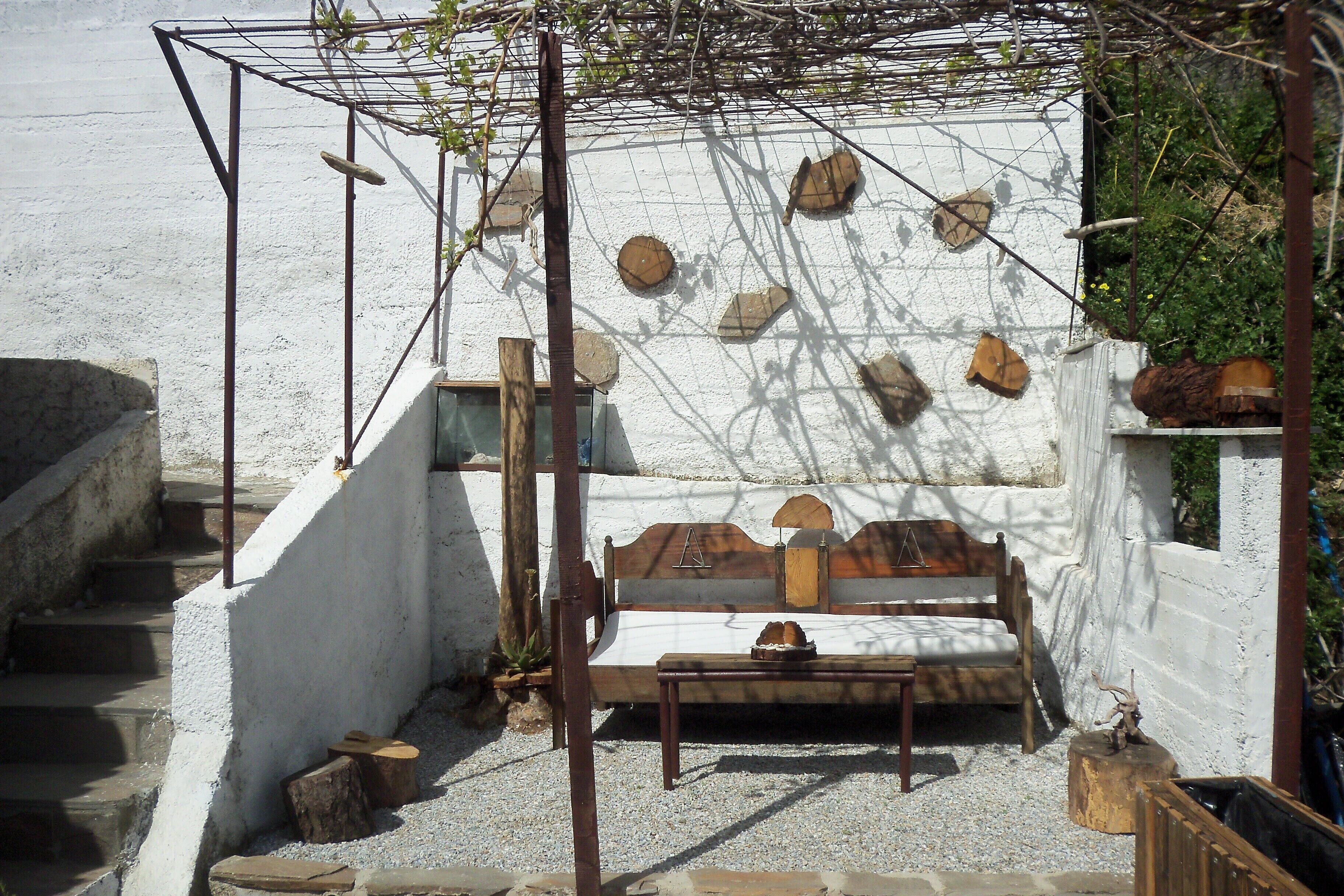 Un'area esterna rustica con una panchina in legno, un tavolino e una struttura a pergola in metallo.