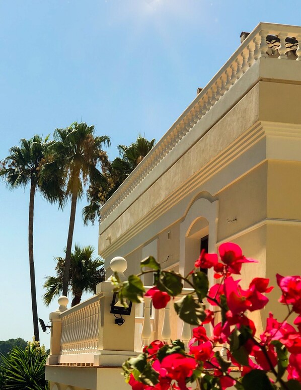 A building with a balcony, palm trees, and red flowers. - Directly on the Golf course.Huge Golf and Spa Mansion 8 min from Puerto Banus (Benahavís)
