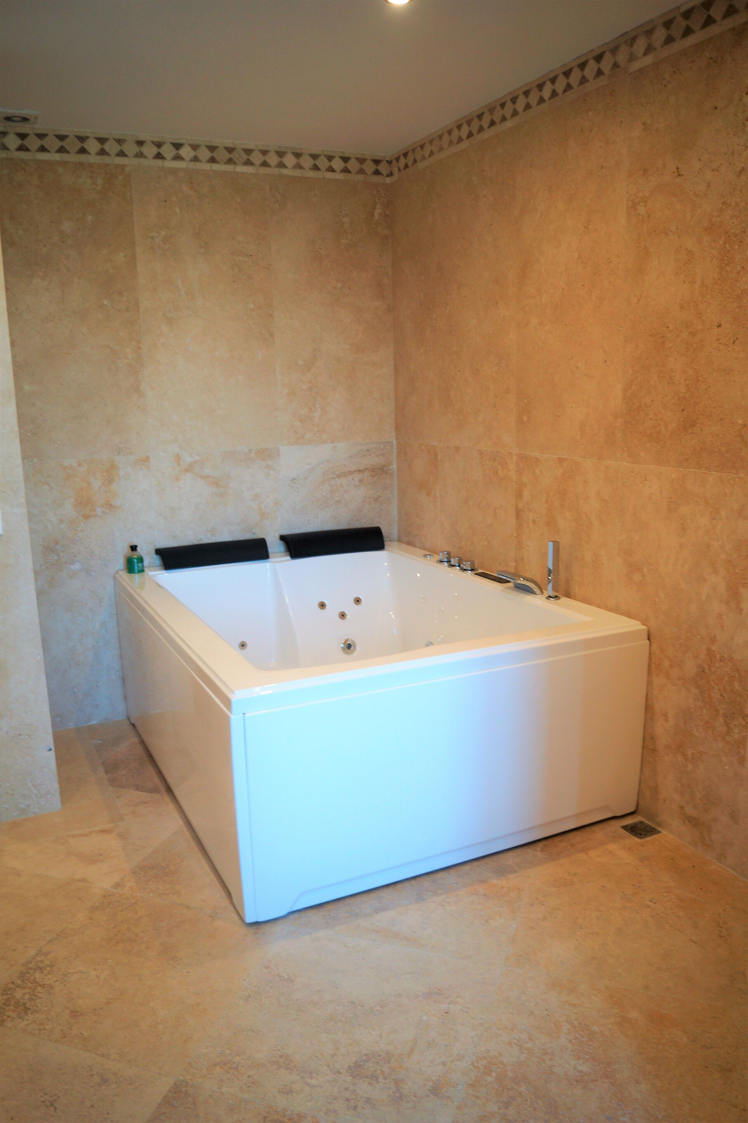 Una vasca da bagno bianca in un bagno con piastrelle beige su pareti e pavimento.