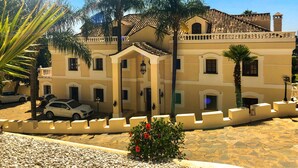 A multi-story building with a tiled roof, a central entrance with a canopy, and a paved courtyard with pebbles and a small red flower bush. - Directly on the Golf course.Huge Golf and Spa Mansion 8 min from Puerto Banus (Benahavís)