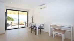 Een moderne kamer met een eettafel, stoelen, een bank, een plafondventilator en een glazen schuifdeur die leidt naar een buitenruimte met uitzicht.