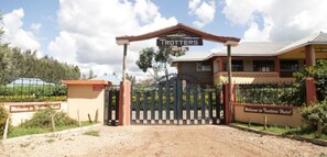 The entrance to Trotters Hotel with a gated driveway and a sign welcoming visitors. - Trotters Hotel (Kabati)