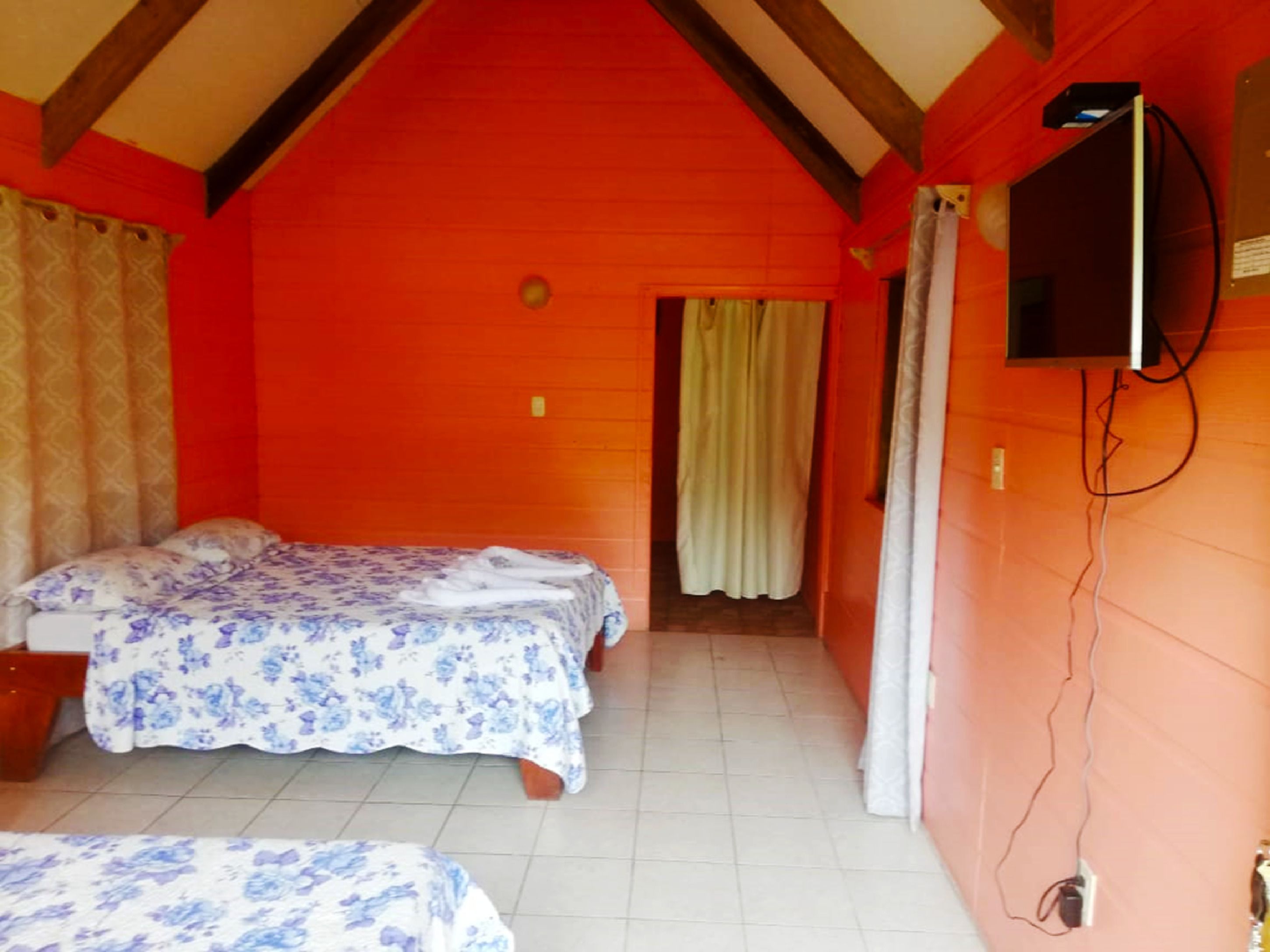 Una habitación con dos camas, un televisor montado en la pared y una ventana con cortinas.