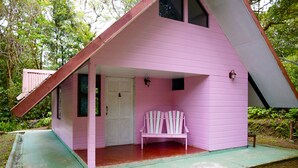 A pink cabin with a sloped roof, a bench outside, and a door. - Cabañas Las Orquideas (Miramar)