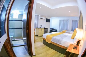 Una habitación de hotel con cama, mesita de noche, lámpara, televisión y vistas al baño.