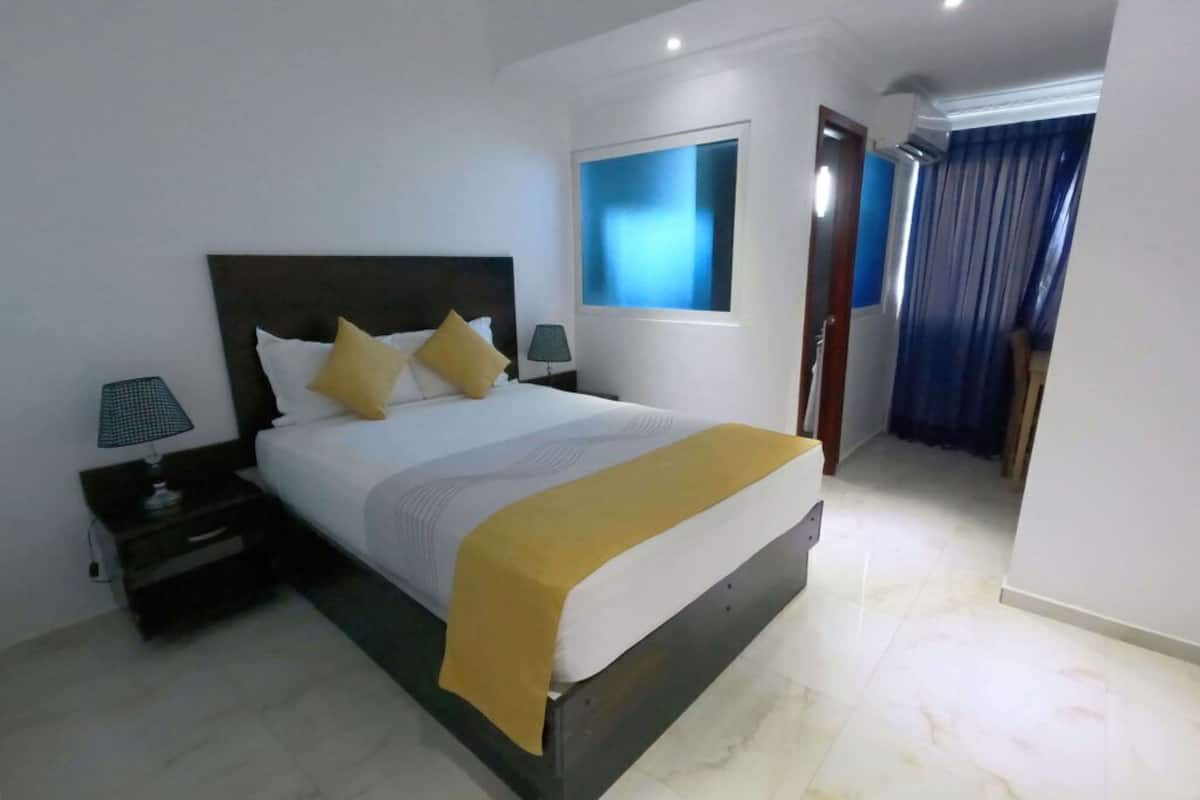 Een moderne slaapkamer met een groot bed, een nachtkastje, een aan de muur bevestigde televisie en uitzicht op een balkon.