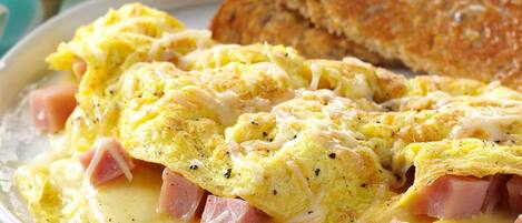 A plate of scrambled eggs with ham and cheese, accompanied by toast and a bowl of fruit.