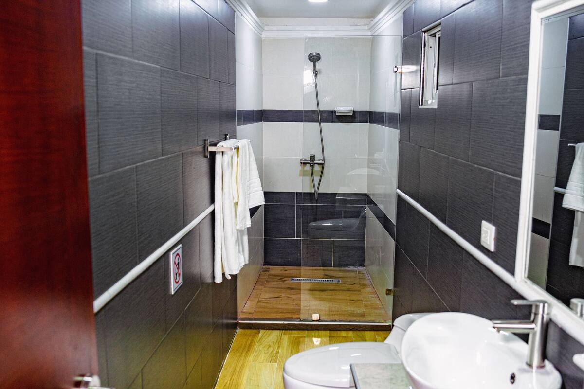 Een smalle badkamer met een houten vloer, een wit wastafelmeubel en een toilet.