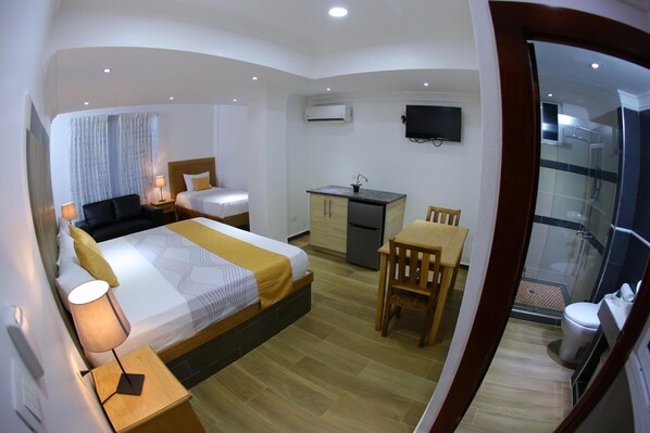 A compact hotel room with a bed, bedside table, lamp, desk, chair, and a small kitchenette. - Hotel Vicentina (Boca Chica)