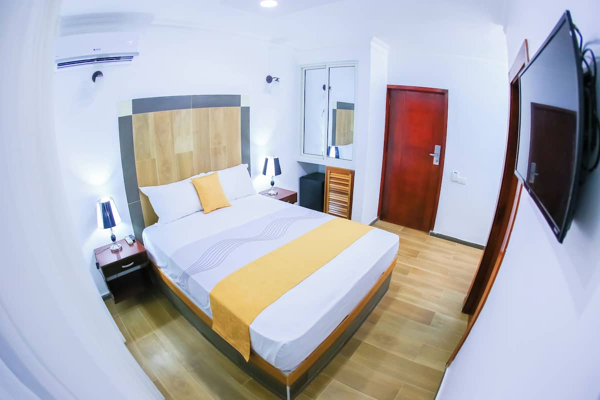 Een hotelkamer met een bed, nachtkastje, lamp, airconditioning, kledingkast en een televisie.