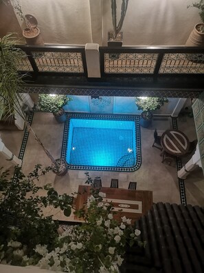 An indoor swimming pool with a tiled floor, surrounded by potted plants and a seating area. - Riad Dalla Santa holiday home (Marrakech)