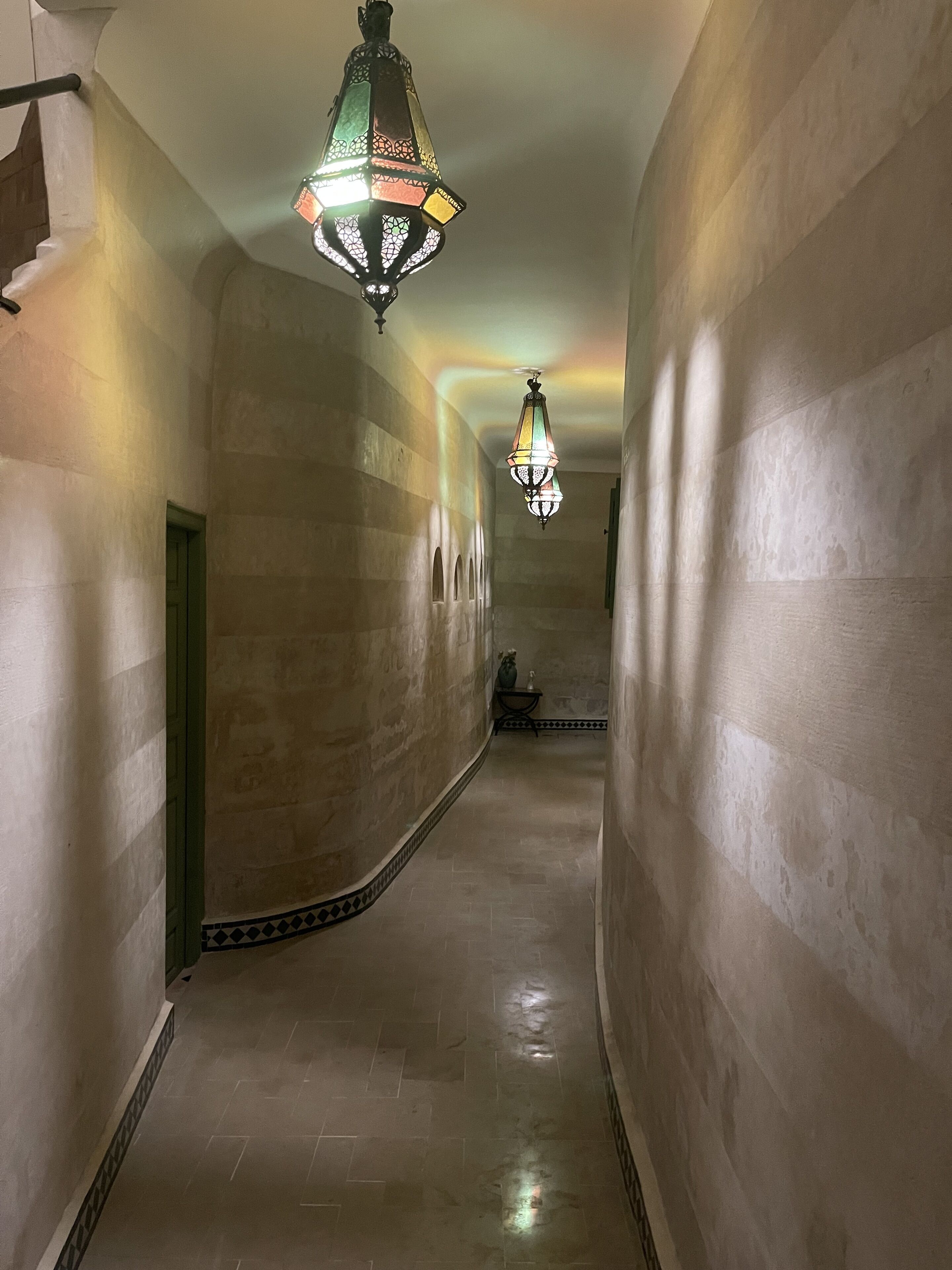 A hallway with patterned walls and a tiled floor, leading to a door at the end.