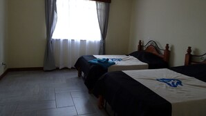 Une chambre avec deux lits simples, une fenêtre avec des rideaux et un sol carrelé.