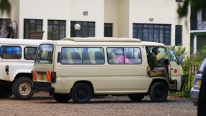 Een beige busje geparkeerd voor een gebouw met meerdere ramen en een deur.