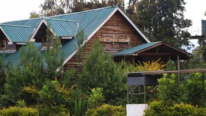 Une cabane en rondins avec un toit végétalisé et une enseigne sur laquelle on peut lire « Village de Karen ».