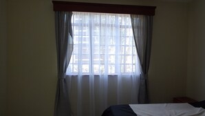 Een slaapkamer met een bed, een raam met gordijnen en uitzicht op bomen.