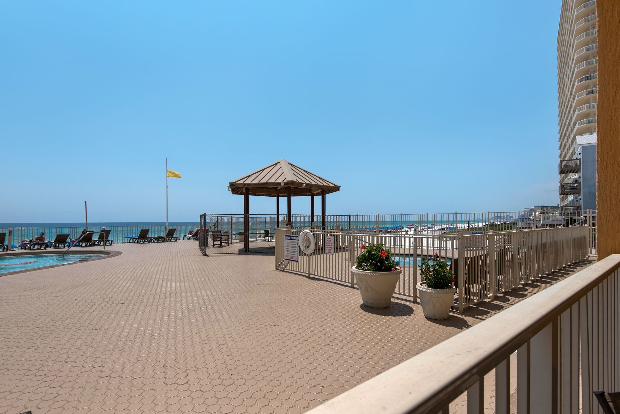 A rooftop pool area with lounge chairs, a gazebo, and a view of the ocean.
