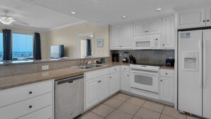 A modern kitchen with white cabinets, a granite countertop, a dishwasher, a stove, a microwave, and a refrigerator.