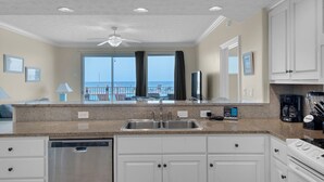 A modern kitchen with a large window, a ceiling fan, and a view of the ocean.