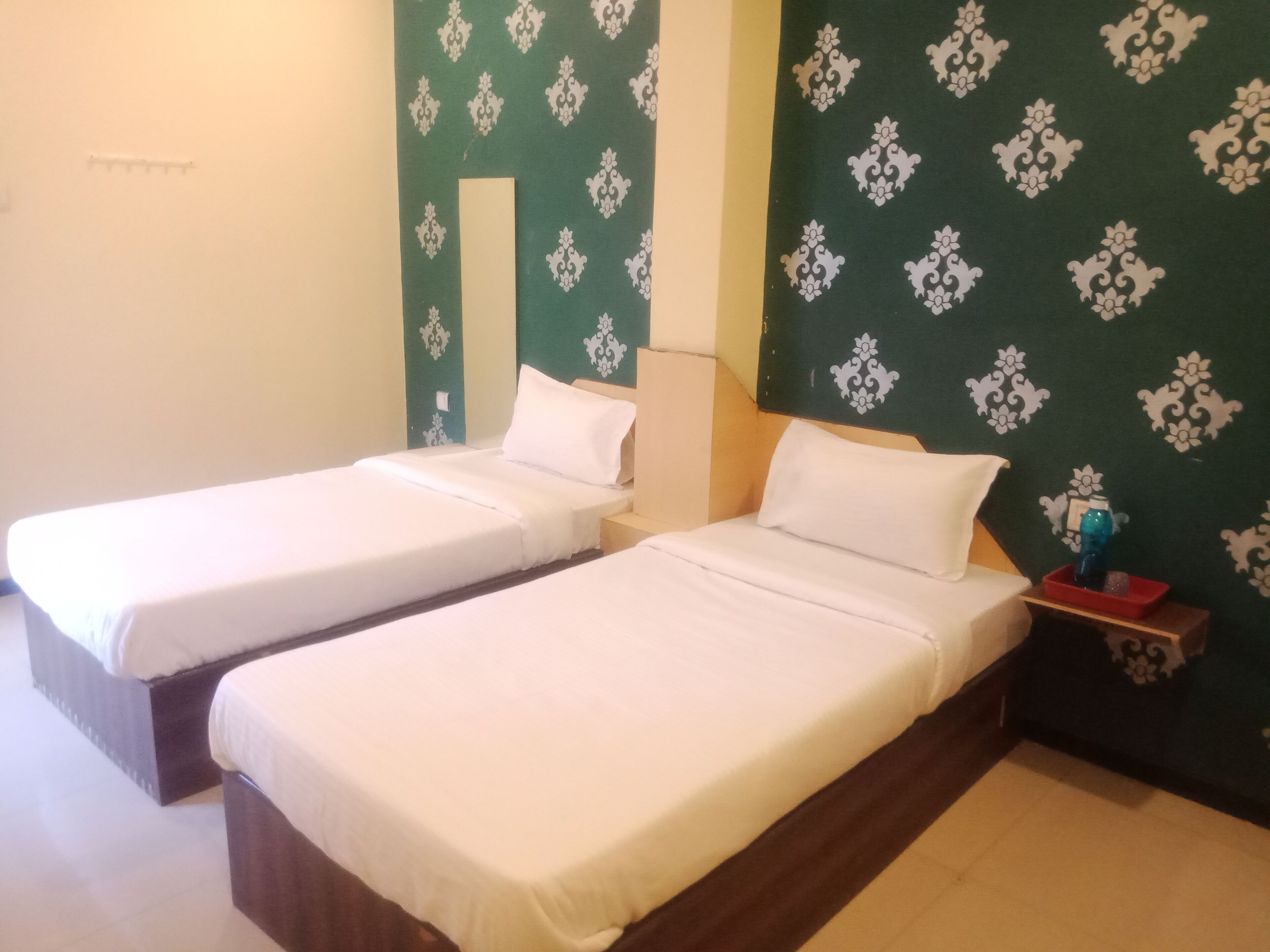 Two single beds with white linens in a room with green patterned wallpaper.