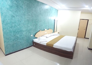 Una habitación de hotel con una cama, una mesita de noche, una lámpara de pared y una puerta.