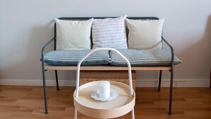 A room with a wooden floor, a metal-framed sofa with striped cushions, and a small wooden table with a cup and saucer. - LULLABY HOUSE LAZISE (Lazise)