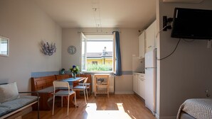 A compact room with a bed, a small dining table with chairs, a kitchenette, and a window with curtains. - LULLABY HOUSE LAZISE (Lazise)