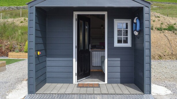 A small, dark blue building with a door open, revealing a kitchen area with a sink and countertop.