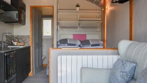 A compact hotel room with a kitchenette, a bed with a headboard, and a seating area with a sofa.