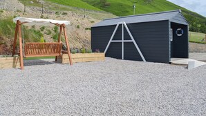 A gravel area with a wooden swing set and a black shed with a lifebuoy on the door.