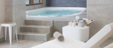 Un spa moderno con una bañera de hidromasaje, sillones blancos y una mesita.