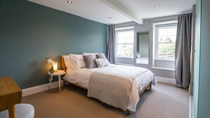 Un dormitorio con cama, una mesita de noche con lámpara, una ventana con cortinas y vistas al exterior.