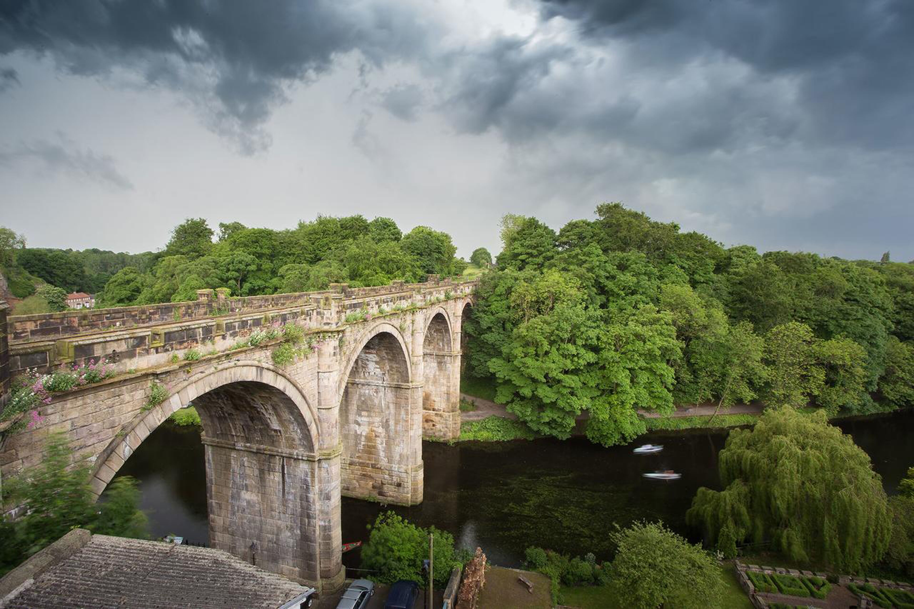 A stone bridge with arches over a river, surrounded by lush greenery and trees.