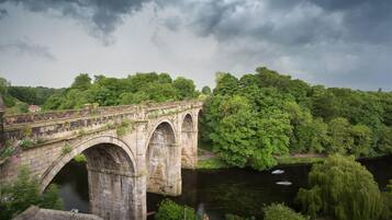A stone bridge with arches over a river, surrounded by lush greenery and trees.