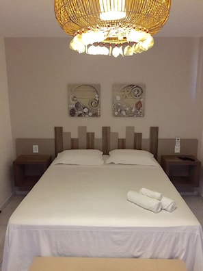 Una habitación de hotel con una cama, dos mesitas de noche, una lámpara de pared y dos piezas decorativas en la pared.