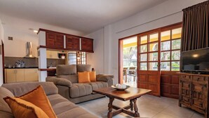 A living room with a sofa, a coffee table, and a TV. There is a kitchen in the background with cabinets and a stove. - GC0285 Holiday house with shared pool in Mogán (Mogán)