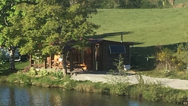 Een rustieke houten hut aan een meer, met een terras en een klein tuinhuisje.