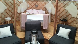 Een gezellig interieur van een joert met een bed, twee banken, een klein krukje en een tafel met een lamp.