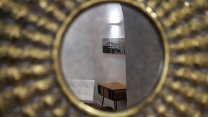 Une pièce dont un mur est recouvert de miroirs, reflétant un lit, une petite table et un tableau accroché au mur.