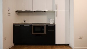 Une cuisine compacte avec des meubles hauts blancs, un meuble bas noir, un four à micro-ondes et un réfrigérateur.