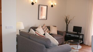 A living room with a grey sofa, a small round table, a TV on a stand, and a lamp. - Lovely 2 bedrooms apartment in Torre Soli Nou (San Jaime Mediterráneo)