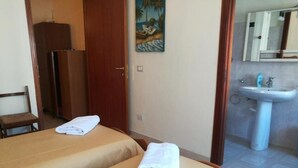 Habitación de hotel con dos camas, un baño con lavamanos y un cuadro en la pared.