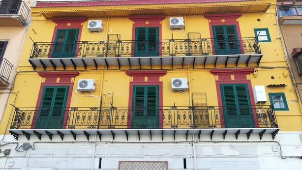 Un edificio de varios pisos con balcones, unidades de aire acondicionado y contraventanas verdes.