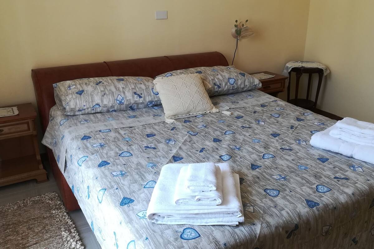 A neatly made bed with a patterned bedspread, a bedside table with a lamp, and a small wooden nightstand.