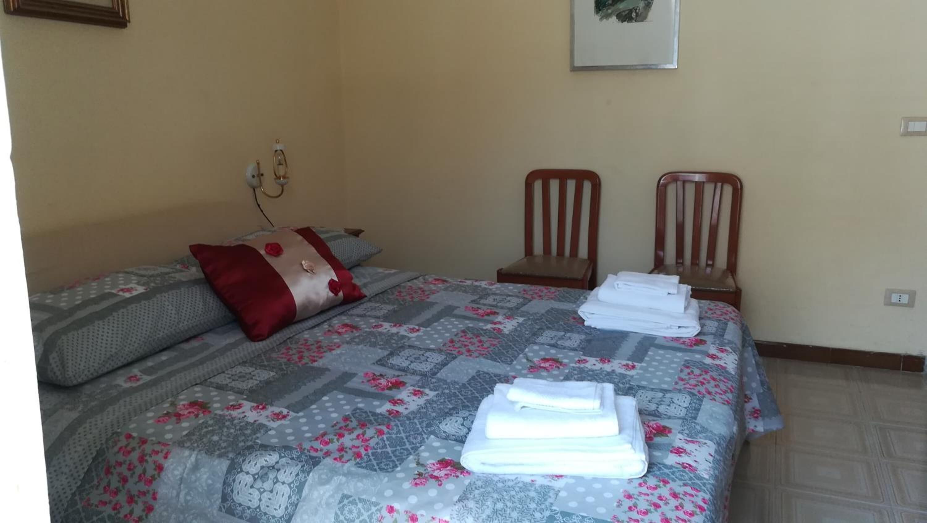Una cama bien hecha con colcha estampada, dos almohadas y toallas dobladas sobre un cabecero de madera.