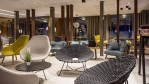 Un área de descanso moderna con mobiliario contemporáneo, incluyendo un sillón amarillo, un sofá gris y una silla tejida negra.
