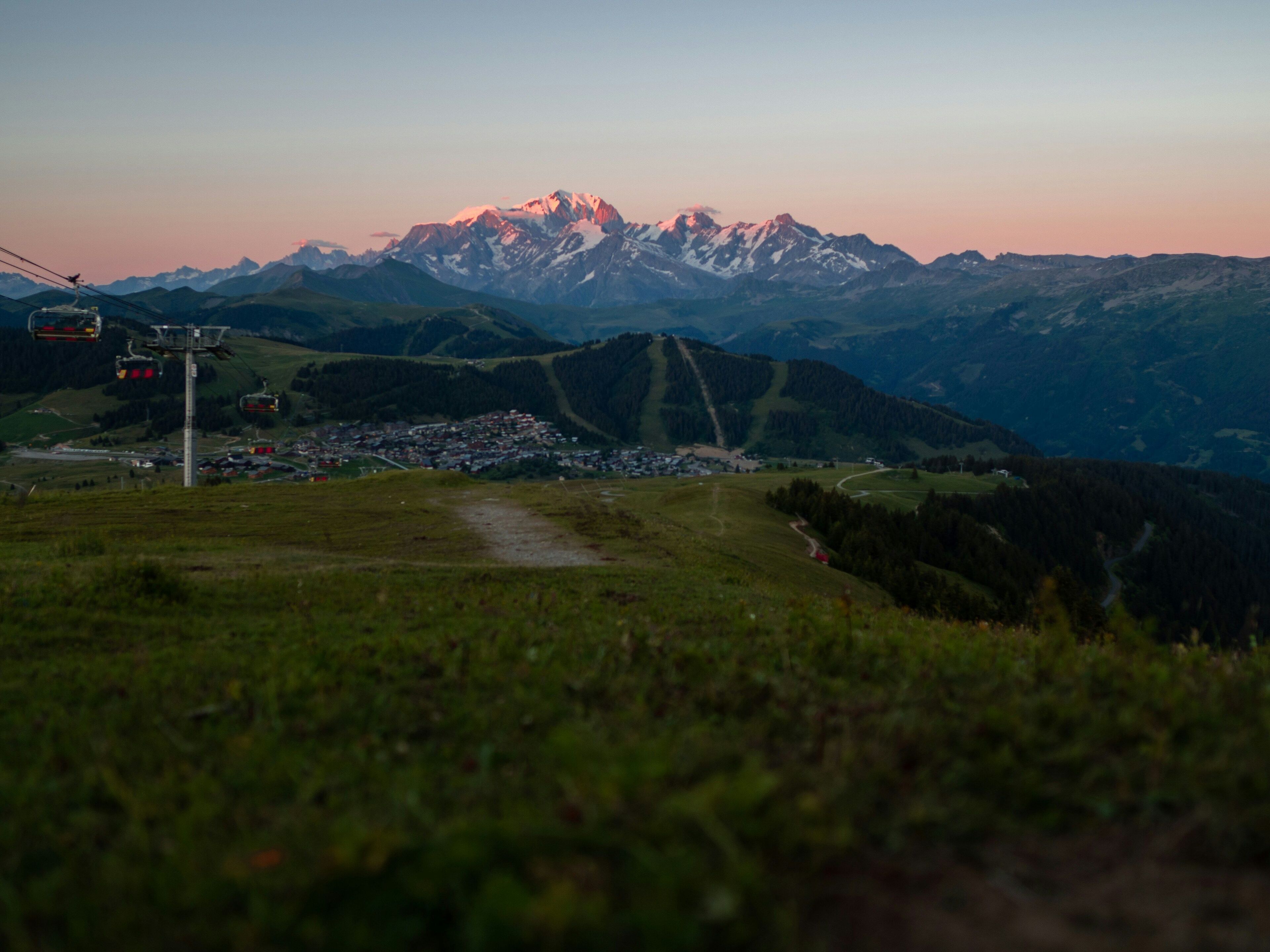 A mountain landscape with a ski lift, a village, and a clear sky.