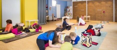 A brightly colored room with children and adults engaged in various activities, including reading and playing.