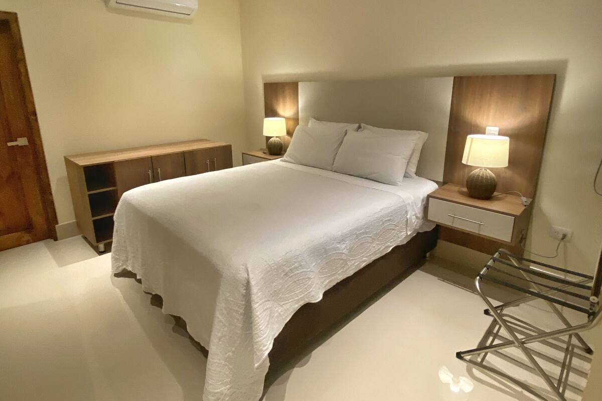 Ein Schlafzimmer mit einem Bett, Nachttischlampen, einem Holfnachtkästchen, einem Einbauschrank und einer Wand-Klimaanlage.