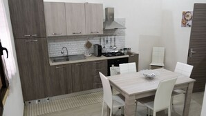 A modern kitchen with grey cabinets, a stainless steel range hood, and a dining area with a light wood table and white chairs. - A stone's throw from downtown and the sea modern comfort and the scent of Marsala bread (Marsala)